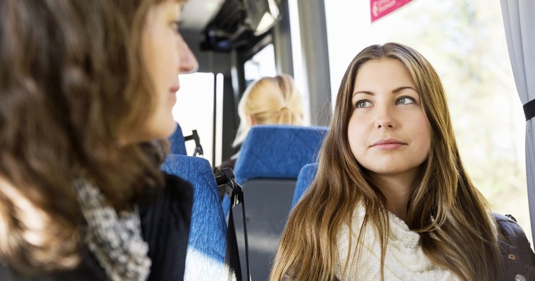 en ung kvinna sitter på en buss. I förgrunden en annan person i oskärpa