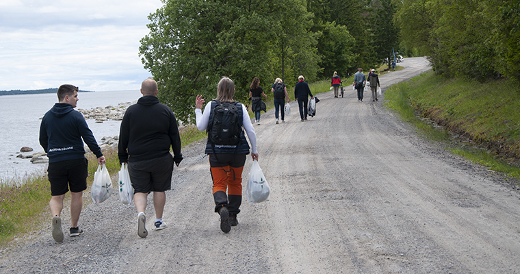 ett tiotal personer ses bakifrån gå längs en grusväg med plastpåsar i händerna