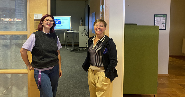 Två glada kvinnor som står vid en öppen dörr in till en möteslokal.