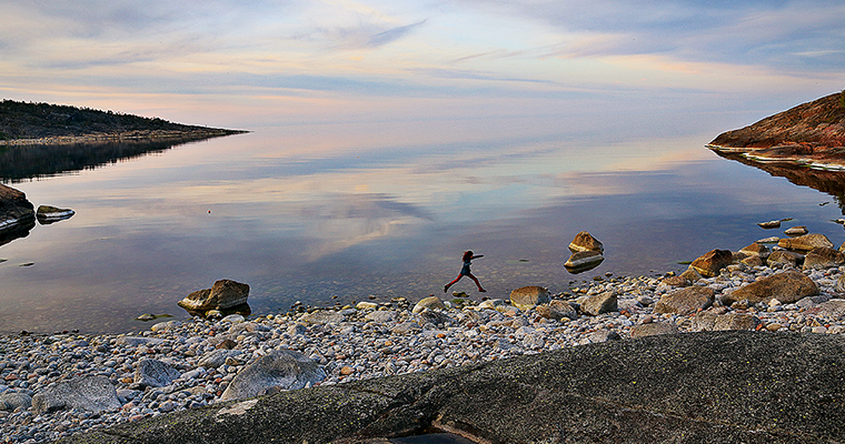 En person gör ett skutt på en stenstrand med havet i bakgrunden