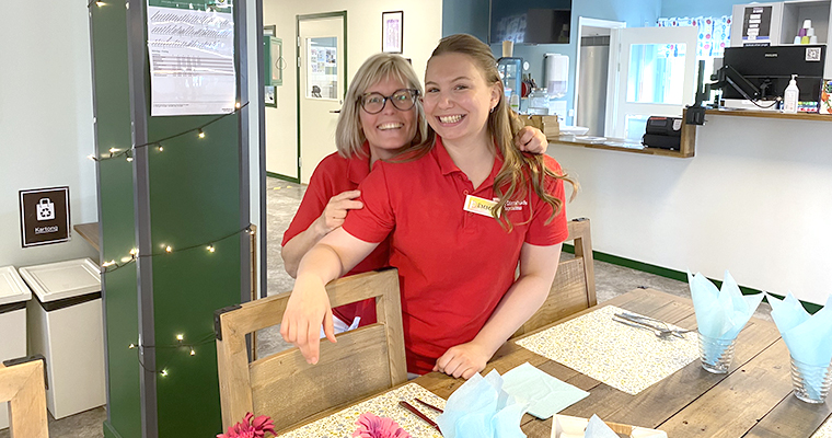 Två glada kvinnor dukar i ett fik.