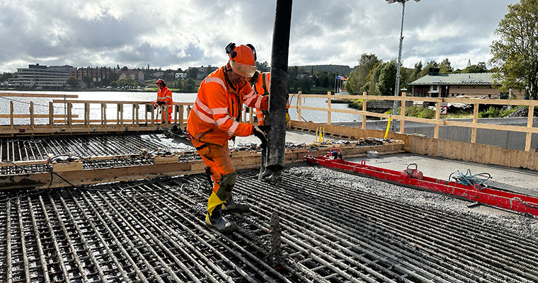 en person med orange arbetskläder håller en stor slang över en stor yta med armeringsjärn