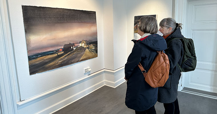 två kvinnor står och betraktar en tavla