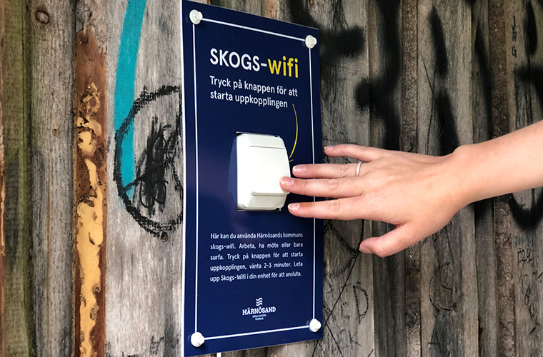 En hand trycker på en knapp mitt i en skylt som handlar om skogs-wifi.