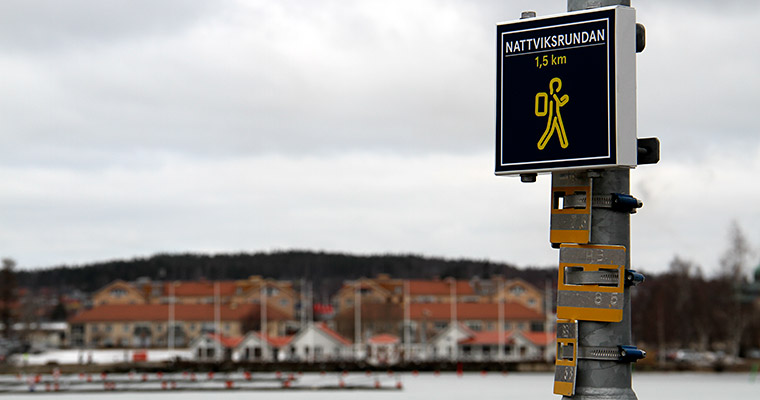 En skylt med texten "Nattviksrundan", i bakgrunden syns Nattviken och sjöbodar.