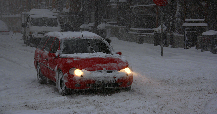 Röd bil som kör i snömodd på en stadsgata