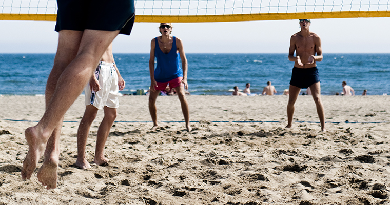 fyra personer spelar becahvolley med havet i bakgrunden