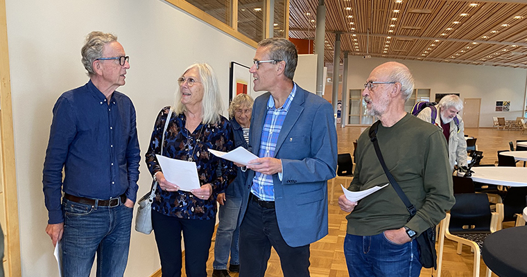 Fyra personer står i en stor lokal och samtalar.