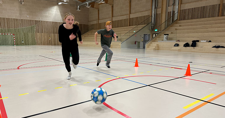 två barn springer med en fotboll i en idrottshall