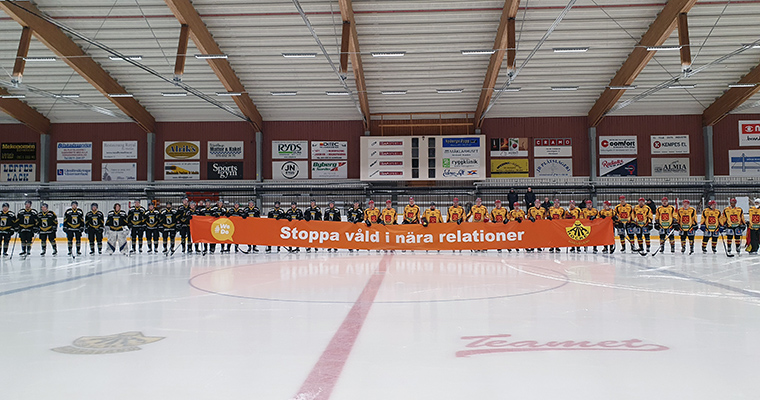 Hockeyspelare på isen med en banderoll med texten "Stoppa våld i nära relationer".