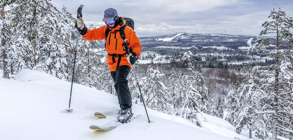 en skidåkare med orange jacka kommer precis upp på ett berg med en vy över ett vinterlandskap i bakgrunden