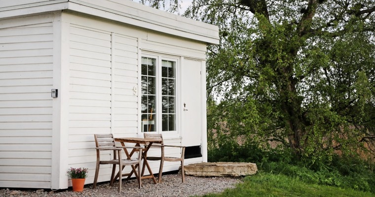 en mindre vitt hus med två trädgårdsstolar och ett bord framför