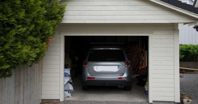 ett garage med öppen port. I garaget står en grå bil