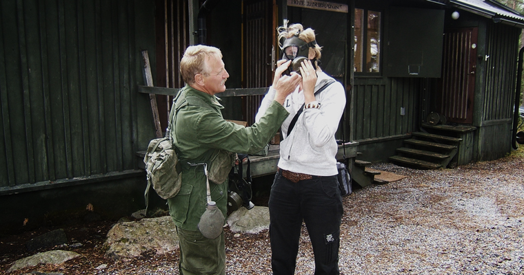 Guide iklädd soldatmundering hjälper till med att sätta på gasmask på besökare