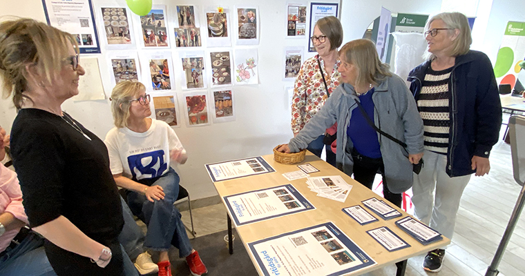 Tre kvinnor tillar intresserat på informationsmaterialet på ett monterbord.