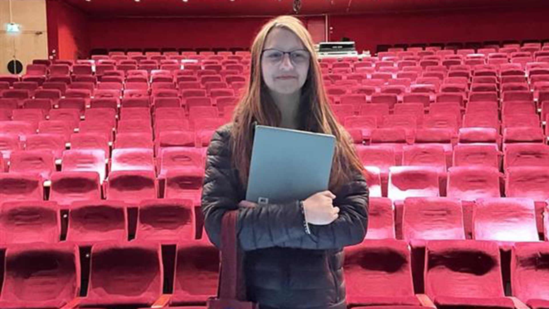 Porträttbild på Amanda ståendes på teatern med salongens röda stolar i bakgrunden
