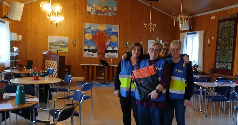 Tre leende kvinnor i reflexvästar står inomhus.