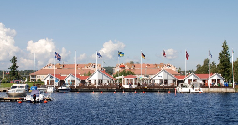 några sammanhängande byggnader som ligger vid vattnet. Vid byggnaderna står en rad med flaggstänger.