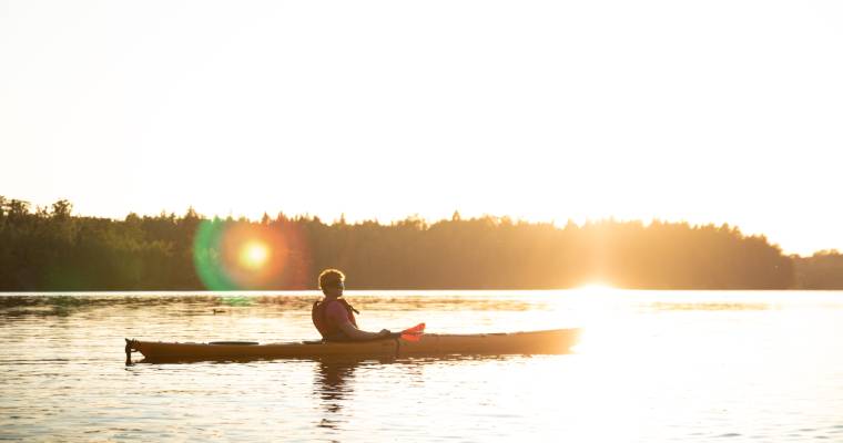 Människa paddlar kanot i soluppgång på lugnt hav.