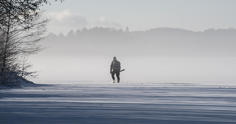 En man med isborr på en frusen sjö. 
