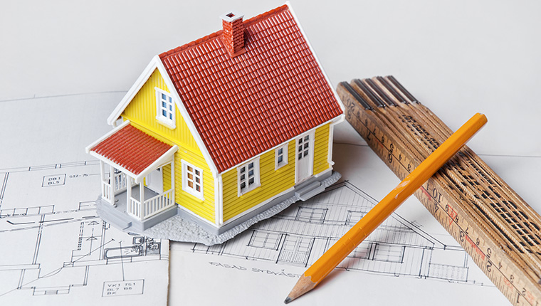 Modell av ett hus, en penna och en tumstock på en byggnadsritning