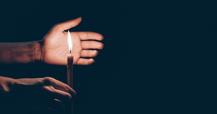 Bild av en hand som skyddar lågan på ett stearinljus.