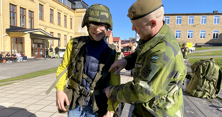 En man i grön uniform hjälper en gymnasieelev att ta på sig militär utrustning.