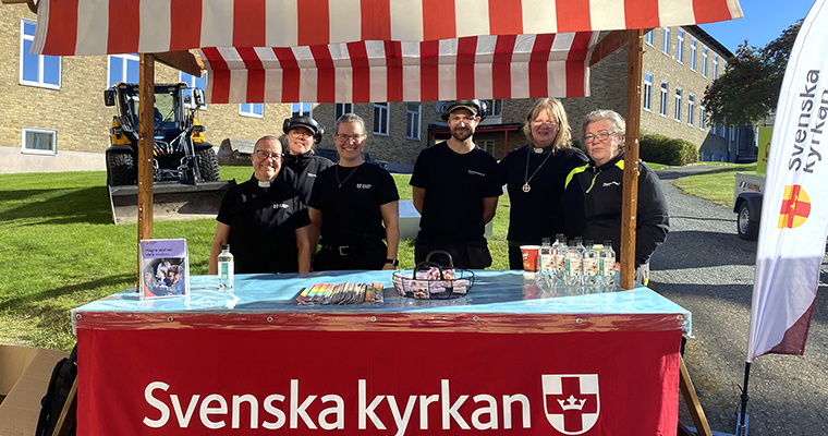Sex glada personer vid ett marknadsstånd med texten Svenska kyrkan.