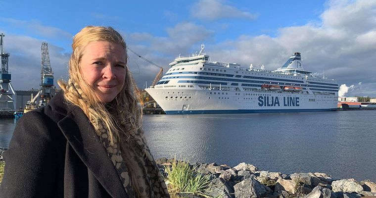 en kvinna står i förgrunden med ett stort fartyg som det står Silja Line på i bakgrunden