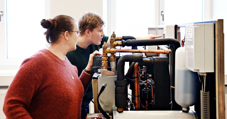 En man och en kvinna tittar nyfiket in i en värmecentral och läser av en mätare.