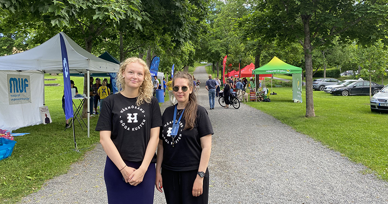 Två kvinnor i stadsparken med tält från olika politiska partier i bakgrunden.