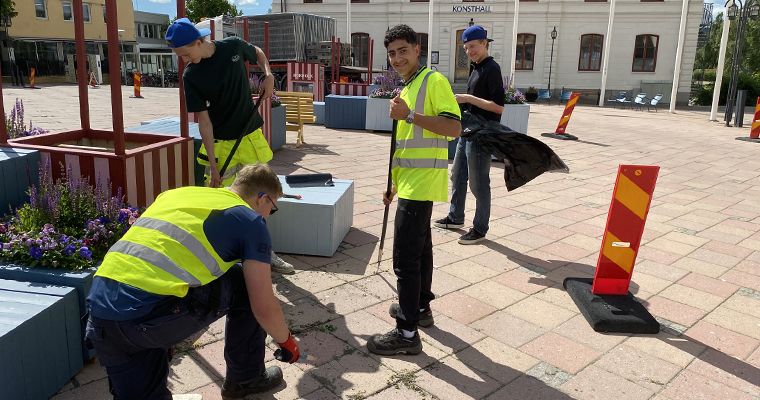 Fyra unga killar med varselvästar rensar ogräs på torget.