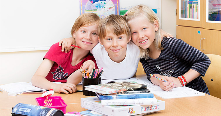Tre glada skolbarn sitter vid ett bord.