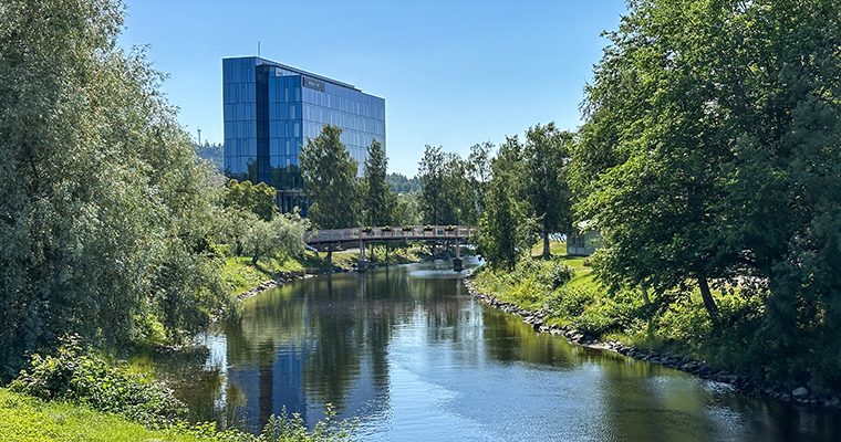 Hernö Gin Hotel sticker upp i fonden. I förgrunden träd och grönska vid kanalen.