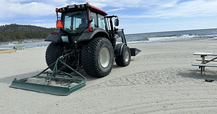 en traktor med en harv kör på en sandstrand vid havet