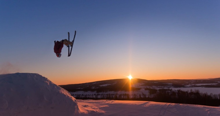 en skidåkare gör ett hopp med en solnedgång i bakgrunden