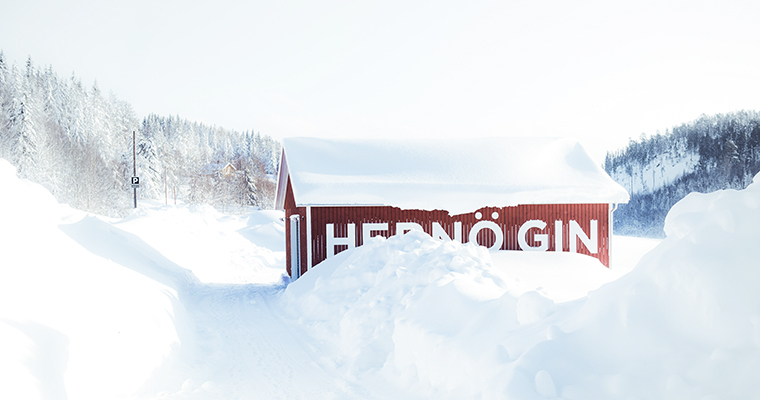 En röd liten byggnad med texten Hernö gin på väggen i ett landskap med väldigt mycket snö