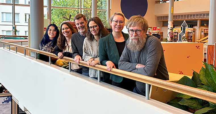 flera personer på rad som lutar sig över ett räcke och tittar in i kameran.