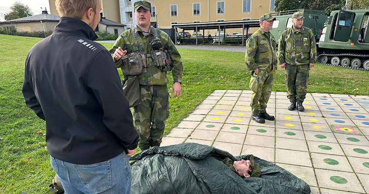 en militär pratar med en ung kille. På marken ligger en annan militär i en sovsäck.