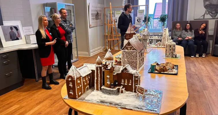 Ett rum där det pågår en pepparkakstävling på Härnösands gymnasium, till vänster är det en jury på 4 personer och i mitten av rummet är det ett bord med pepparkakshus och längst bort är det elever