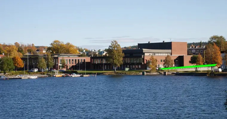 vy över en stor röd byggnad med vatten i förgrunden. intill byggnaden går ett grönt streck