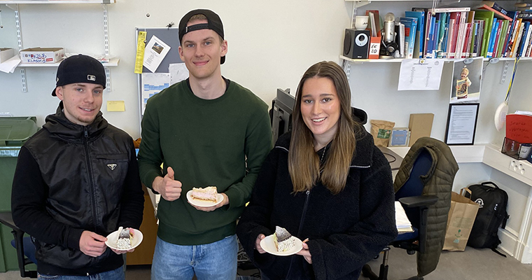 Tre glada gymnasister står med varsin tårtbit på en assiett.