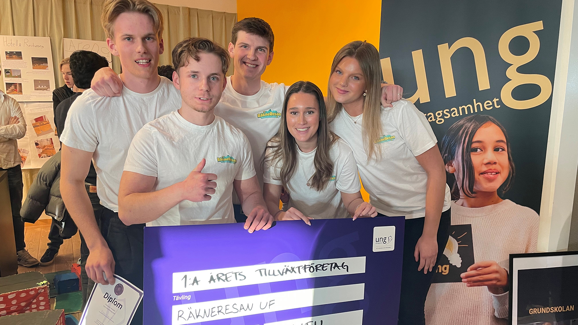 Fem glada ungdomar som poserar vid en stor prischeck. 