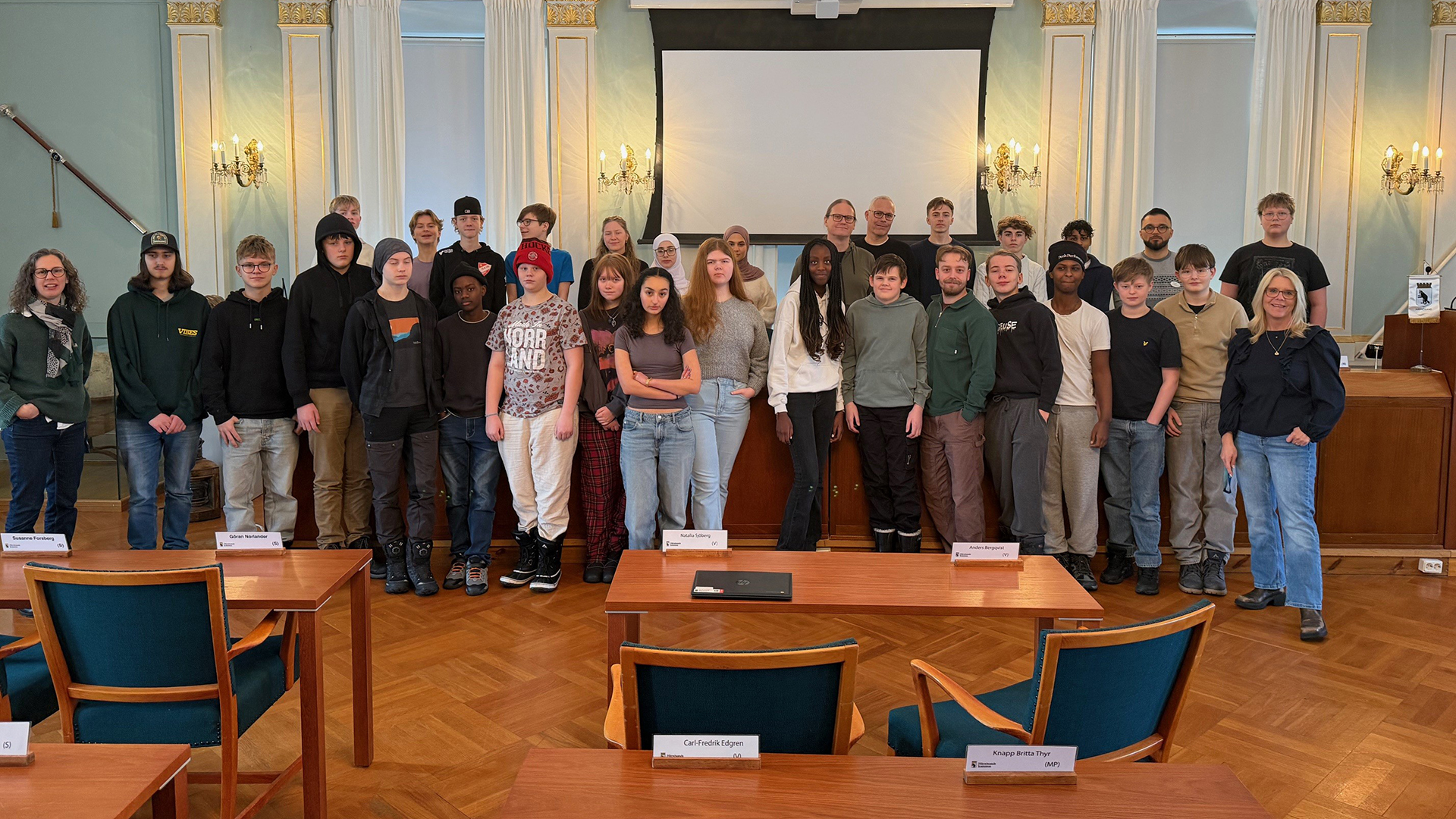 gruppbild på flera elever som står i en stor grupp vid podiet i kommunfullmäktigesalen
