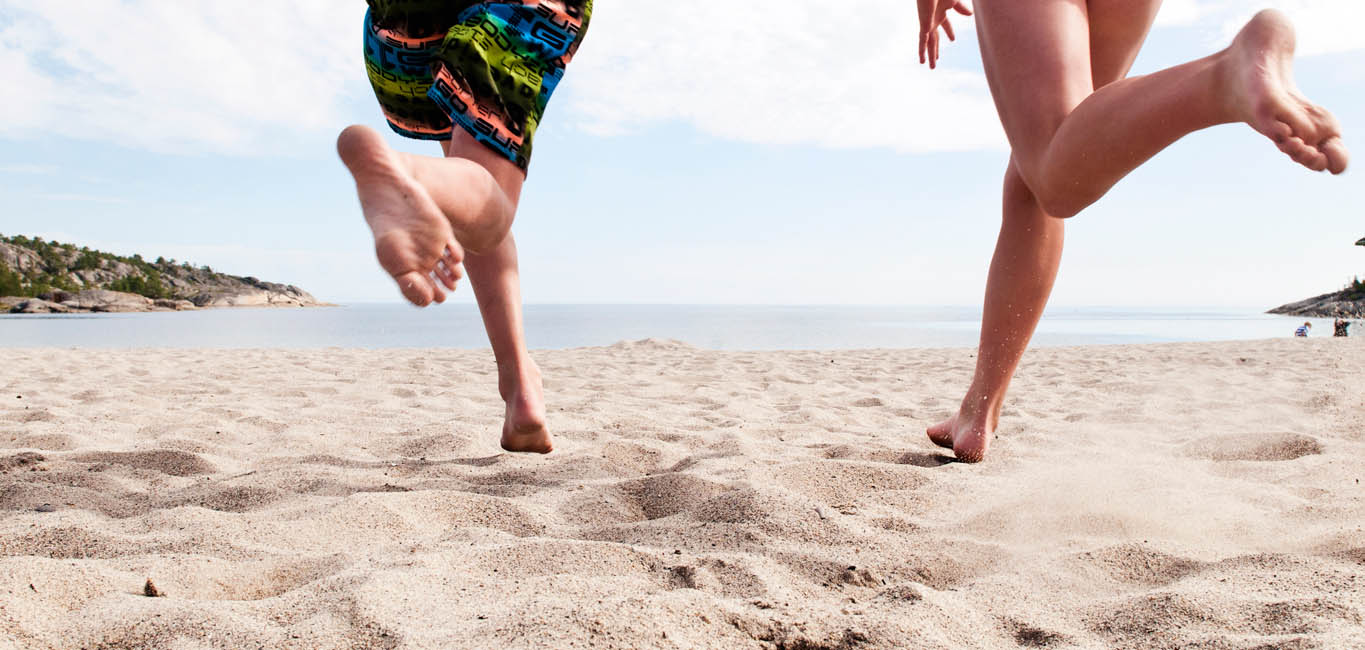 en sandstrand där man ser benen på två personer som springer mot vattnet