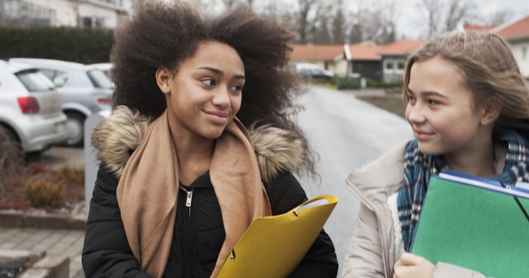 två flickor som är på varsin mapp går på en väg