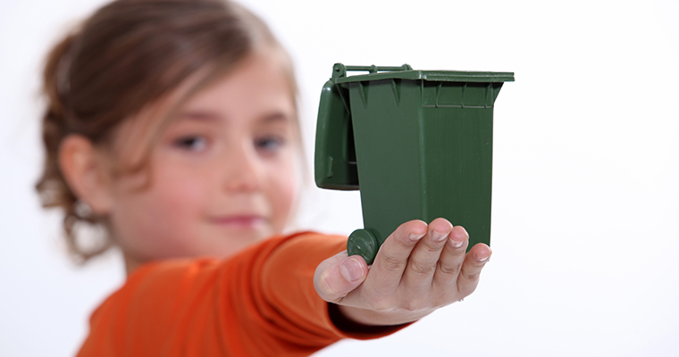 Liten flicka med en miniatyr av en soptunna i sin utsträckta hand.