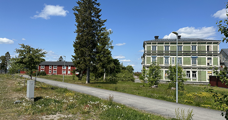 en stadsmiljö med ett stort grönt hus i höger bildkant och lägre röda hus till vänster