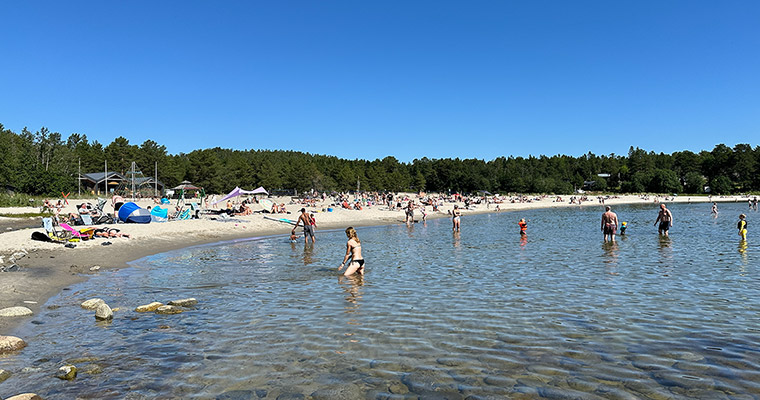 en badstrand med några människor i vattnet och många på stranden