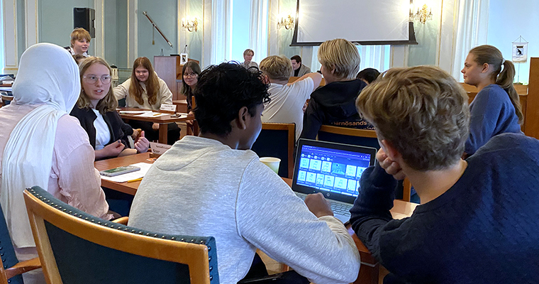 Högstadieelever diskuterar och planerar i en stor möteslokal.